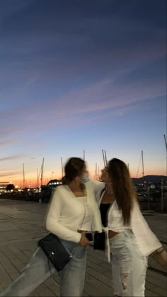 two women are walking down the sidewalk at sunset or dawn with their hands in each other's pockets