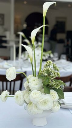 white flowers and greenery in a vase on a table at a formal event or function