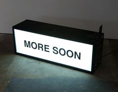 there is a sign that says more soon on the floor in front of a wall