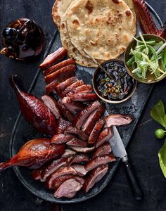 an assortment of meats and vegetables on a platter with bread, olives, peppers, and other condiments