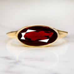 This beautiful and unique solitaire ring features a 2.19ct moval cut red garnet set in a sleek and elegant east west bezel setting! The garnet is a gorgeous rich red hue, and it has a beautiful play of light. The color is rich and luxurious, and it pairs perfectly with the yellow gold setting. The garnet's elongated moval cut adds a unique touch. Combining aspects of the marquise cut and the oval cut, moval cuts are a rare find! The east west setting gives this classic ring a fashionable edge. A Elegant Oval Ruby Ring With Bezel Setting, Elegant Ruby Ring With Bezel Setting, Oval Cabochon, Elegant Oval Cabochon Ruby Ring With Bezel Setting, Oval Faceted Ruby Jewelry, Faceted Oval Ruby Jewelry, Oval Ruby Jewelry With Faceted Detail, Formal Oval Ruby Ring With Polished Finish, Elegant Marquise Ruby Ring, Fine Jewelry Oval Solitaire Ruby Ring