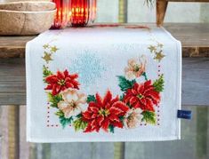 a cross - stitch table runner with poinsettis on it and a candle