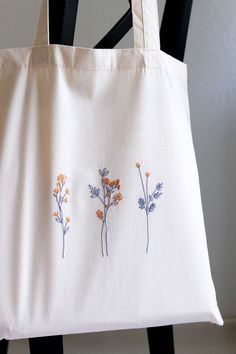 three embroidered flowers on a white tote bag sitting on a black chair in front of a wall