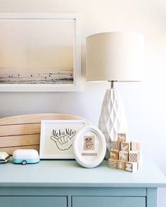 a blue dresser topped with lots of items next to a framed photo and lamp on top of it