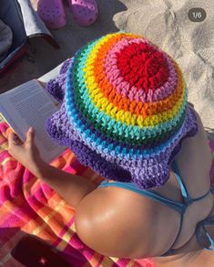 a woman laying on top of a towel next to a book wearing a colorful crocheted hat