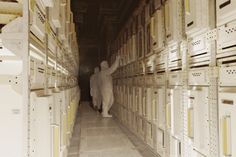 two people are standing in the middle of a room with stacks of boxes on each side