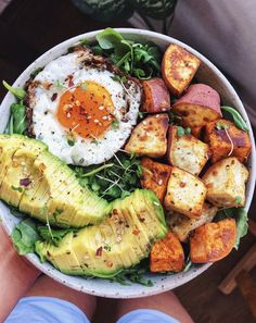 a person holding a bowl filled with vegetables and an egg on top of it's side