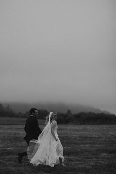 a bride and groom walking through the grass in front of a foggy sky at their wedding