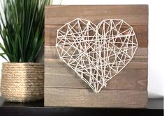 a wooden block with a string heart on it and a potted plant in the background