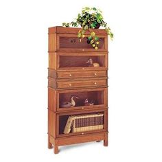 a tall wooden bookcase with drawers and plants on the top, in front of a white background