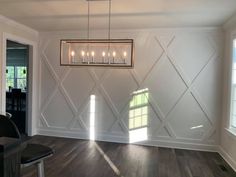 an empty room with wood flooring and white paneled walls that have candles hanging from the chandelier