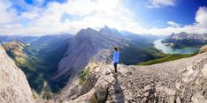 a man standing on top of a mountain looking at the mountains and lakes in the distance