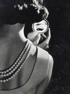 a woman holding a mirror to her face while looking at herself in the mirror with pearls on it