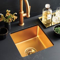 a kitchen sink with gold faucet and black countertop next to it, surrounded by flowers