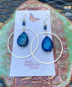 Silver hoop earrings with blue jasper stones. I am over the moon about these beauties! They are large and eye-catching but not too heavy! The stones are royal blue jasper. These earrings are 2 1/2 inches long and 1 1/2 inches wide. The French earwires are sterling silver. All my jewelry comes gift boxed with a custom Shelly Mariposa Design butterfly card ready for gift giving, whether it is a gift for you or someone special. Your satisfaction is very important to me. I make every effort to incor Handmade Blue Hoop Jewelry, Nickel-free Blue Small Hoop Jewelry, Blue Small Hoop Earrings With Matching Set, Blue Bohemian Hoop Earrings With Natural Stones, Bohemian Blue Hoop Earrings With Natural Stones, Bohemian Blue Wire Wrapped Hoop Earrings, Blue Bohemian Small Hoop Jewelry, Bohemian Blue Small Hoop Jewelry, Blue Hoop Jewelry With Natural Stones