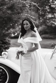 a woman in a wedding dress standing next to an old car wearing a bridal gown