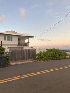 an empty street with a house on the side and ocean in the backround