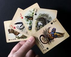 a hand holding four playing cards in front of a black background with animals and birds on them