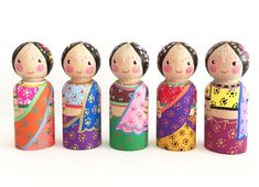 five wooden dolls are lined up on a white surface and one is wearing a colorful dress