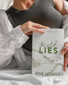 a woman is holding up a book about lies on her stomach while laying in bed