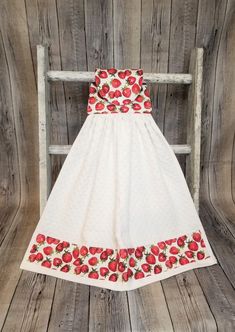 a white dress with strawberries on it is hanging from a wooden ladder in front of a wood wall