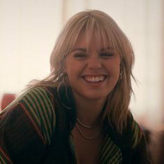 a woman with blonde hair smiling and wearing a green striped shirt in front of a window