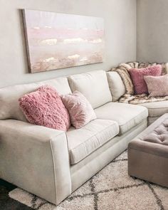 a living room with white couches and pink pillows on the floor, along with a large painting