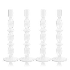 four clear glass candlesticks are lined up in a row on a white background