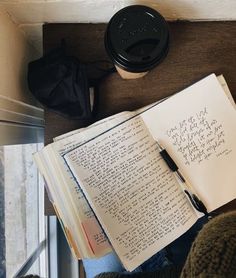 an open book sitting on top of a wooden table next to a cup of coffee