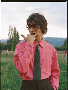 a man in a pink shirt and green tie making the v sign with his hand