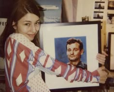 a woman holding up a portrait of a man