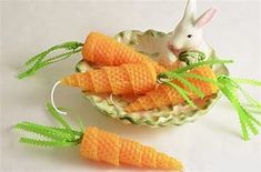 two small carrots are in a bowl with green leaves on the rim and a white rabbit figurine