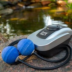 two blue balls sitting on top of a rock next to a pond with water in it