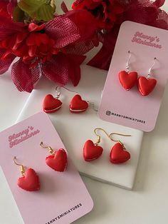 three pairs of heart shaped earrings sitting on top of a card next to red flowers