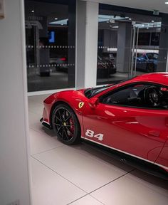 a red sports car parked in a showroom with its door open and the number 84 on it's side