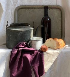 bread and wine are sitting on a table with a white cloth draped over it, next to an old metal pan