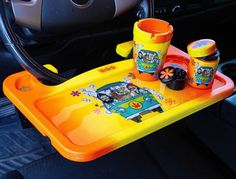 an orange tray with some cups and sauces on it next to a steering wheel