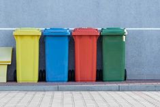 five different colored trash cans lined up in front of a wall with writing on it