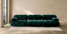 a green couch sitting on top of a hard wood floor next to a large window