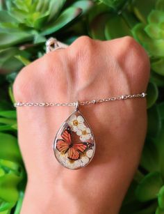 a woman's hand with a butterfly necklace on it and flowers in the background