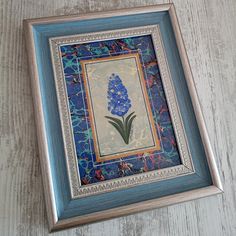 a blue framed painting with flowers in it on a wooden table next to a pair of scissors