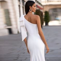 a woman in a white dress is walking down the street with her back to the camera