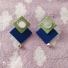 two small square shaped earrings on top of a purple and blue cloth covered tablecloth