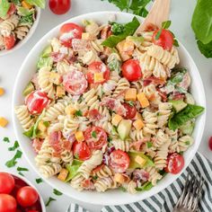 a white bowl filled with pasta salad next to tomatoes and lettuce