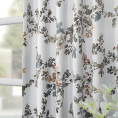 a vase with flowers in it sitting next to a window covered in white and brown curtains