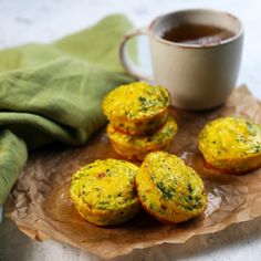 small muffins on a plate next to a cup of tea and green napkin