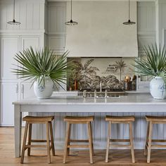 a kitchen island with three stools and two potted plants on the counter top