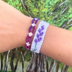 a woman's arm wearing two bracelets with purple and white flowers on them