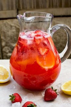 a pitcher filled with liquid next to sliced lemons and strawberries