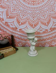 a white vase sitting on top of a green table next to books and a potted plant